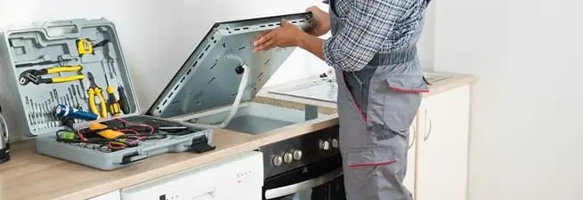 Cooktop repair technician lifting a built-in stovetop for service in Bradenton, FL