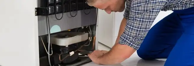 Refrigerator repair technician servicing the compressor and condenser area in Bradenton, FL