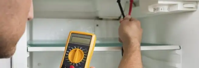 Refrigerator repair technician testing electrical components with a multimeter in Bradenton, FL